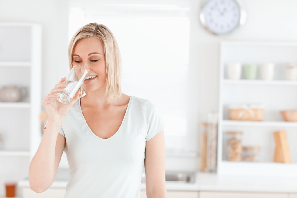 Smiling Woman drinking a glass of water with a slightly blurred background of a kitchen behind her
