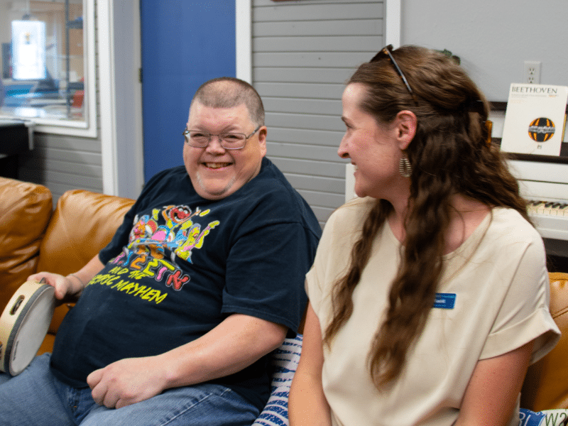 A community center client laughing with a Columbia Ability Alliance employee while playing tamborine